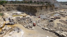 Quarry wall rising behind active machinery and stone stacks