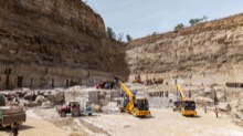 Excavators and trucks operating along the quarry wall