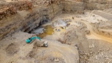 Quarry floor with excavator, trucks, and waterlogged tracks