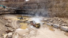 Loaded trucks and an excavator working below the rock face